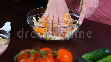 厨房里的一个女人把卷心菜和胡萝卜混合在一起。 白碗里有胡萝卜的卷心菜沙拉